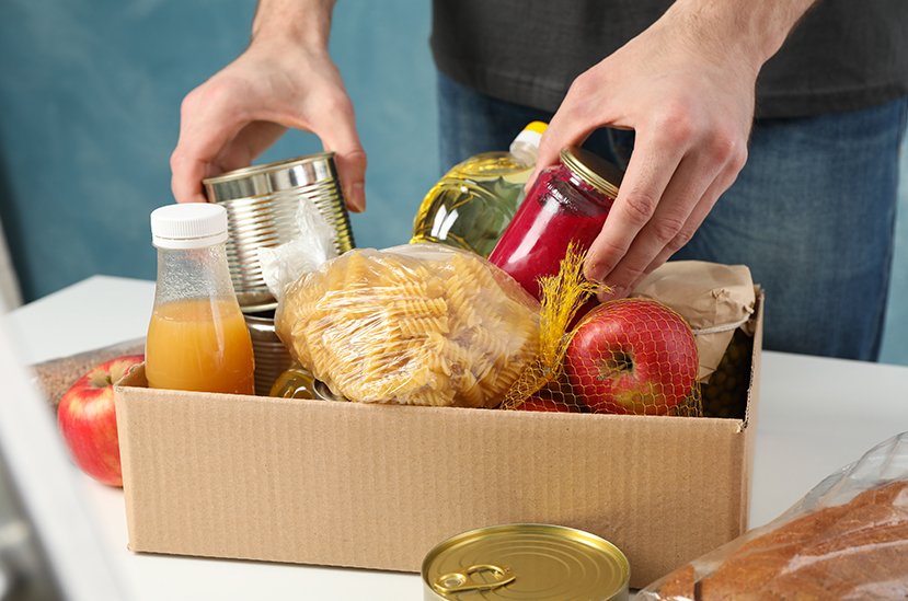 Food Bank. Young man puts groceries in donation box. Volunteer.